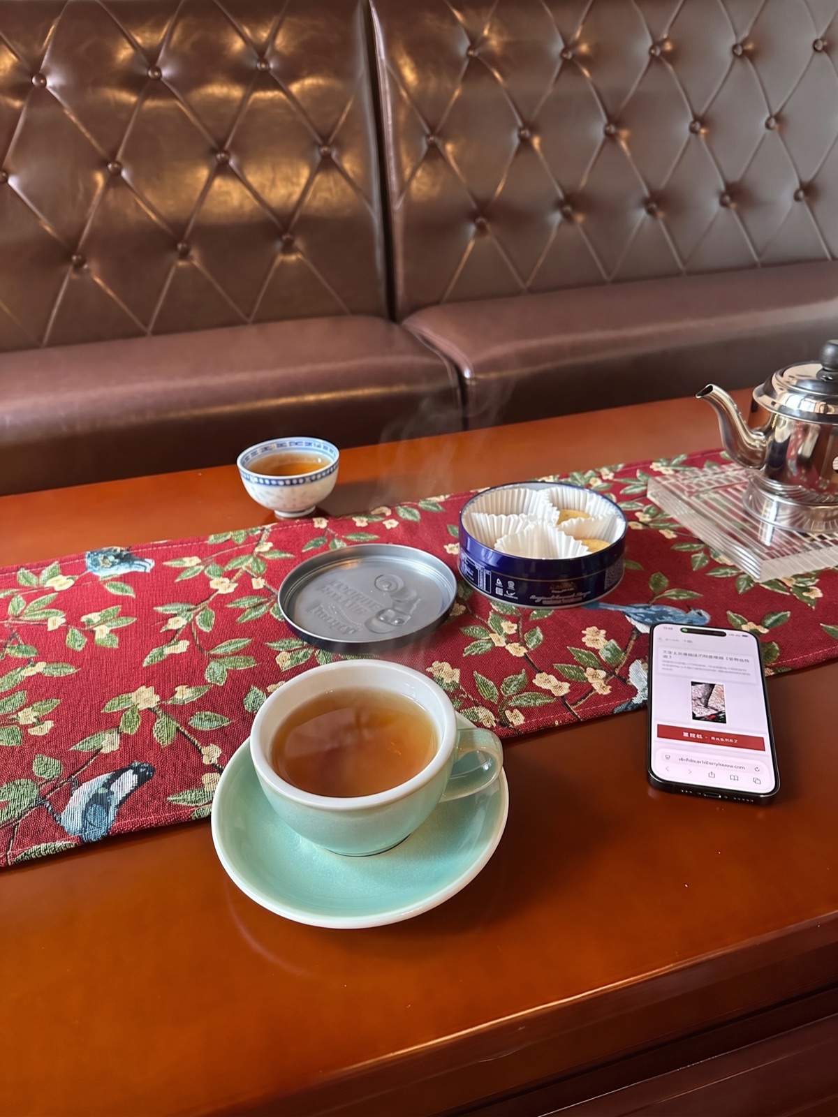 茶樓卡座嘅枱面：一杯熱茶、一個蓋碗、一罐餅，同一部擺喺枱上面嘅電話